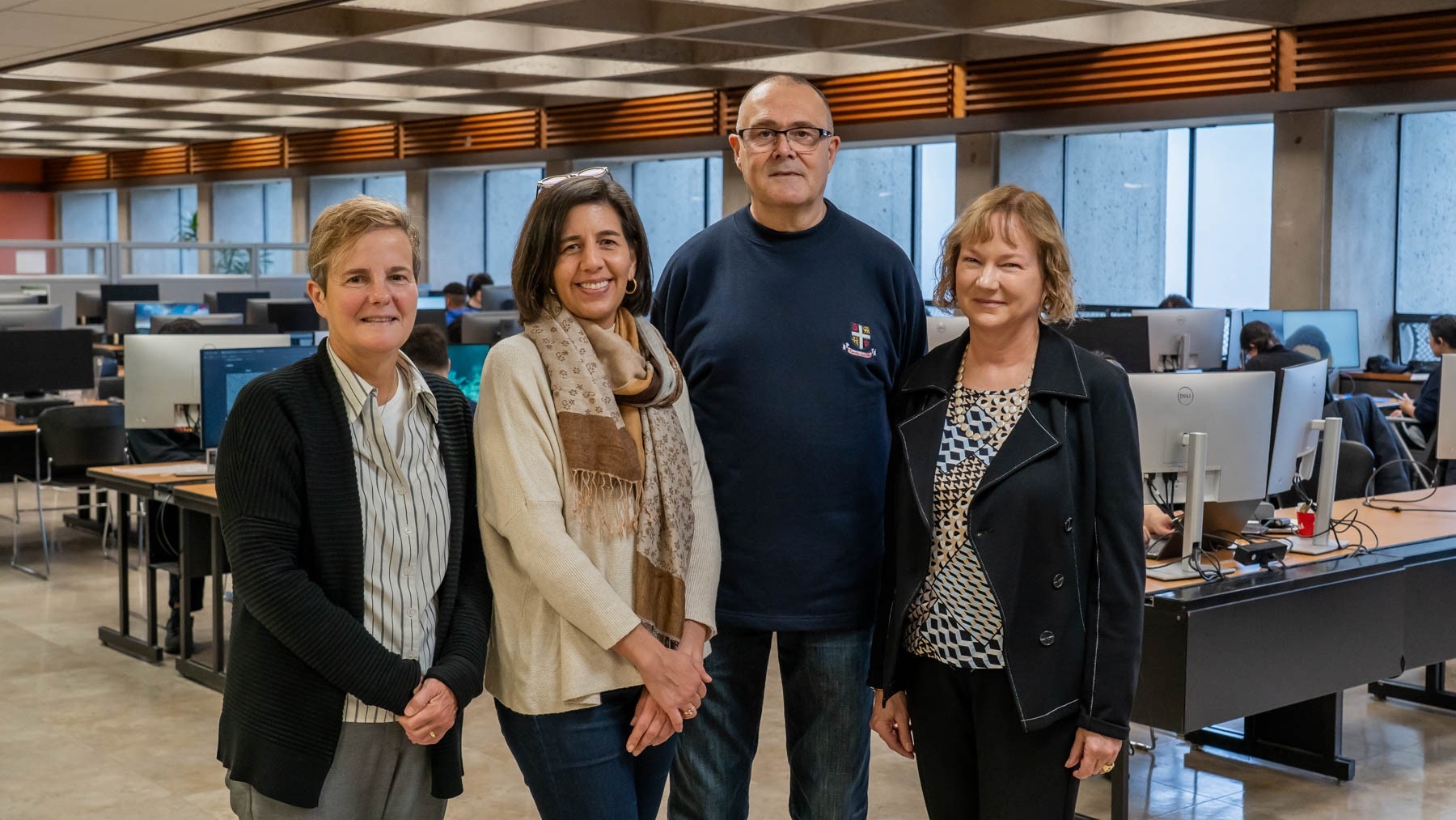 Four people (Gwen Bird, Melek Ortabasi, Malcolm Toms, Natalie Gick) standing together posing in SFU Bennett Library.
