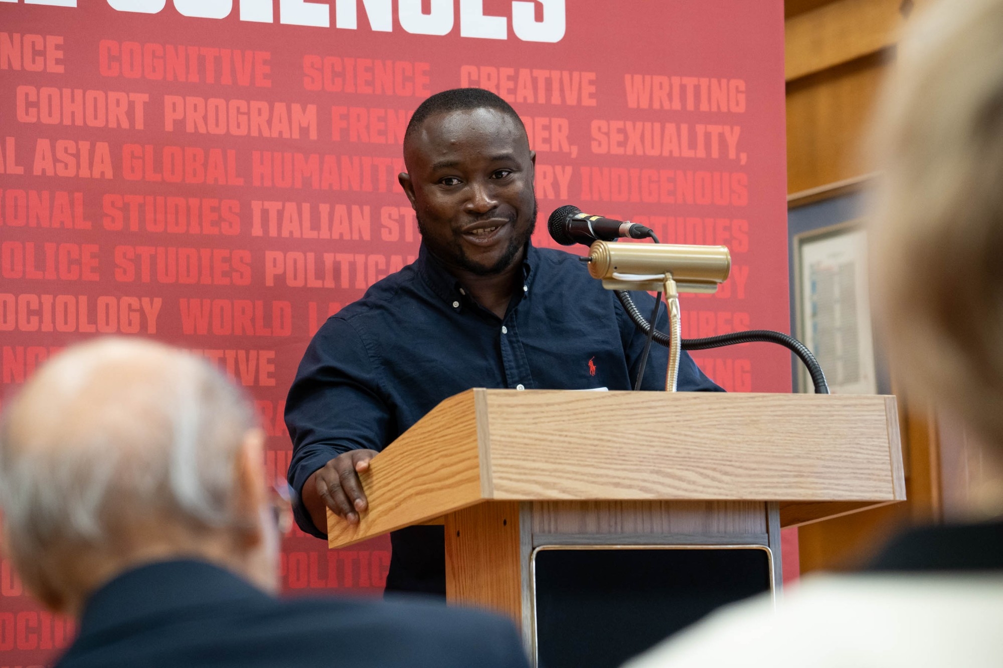 Denis giving a speech at the professorship launch event. He is looking directly at Dr. A.H. Somjee. Denis is wearing a dark blue button down.