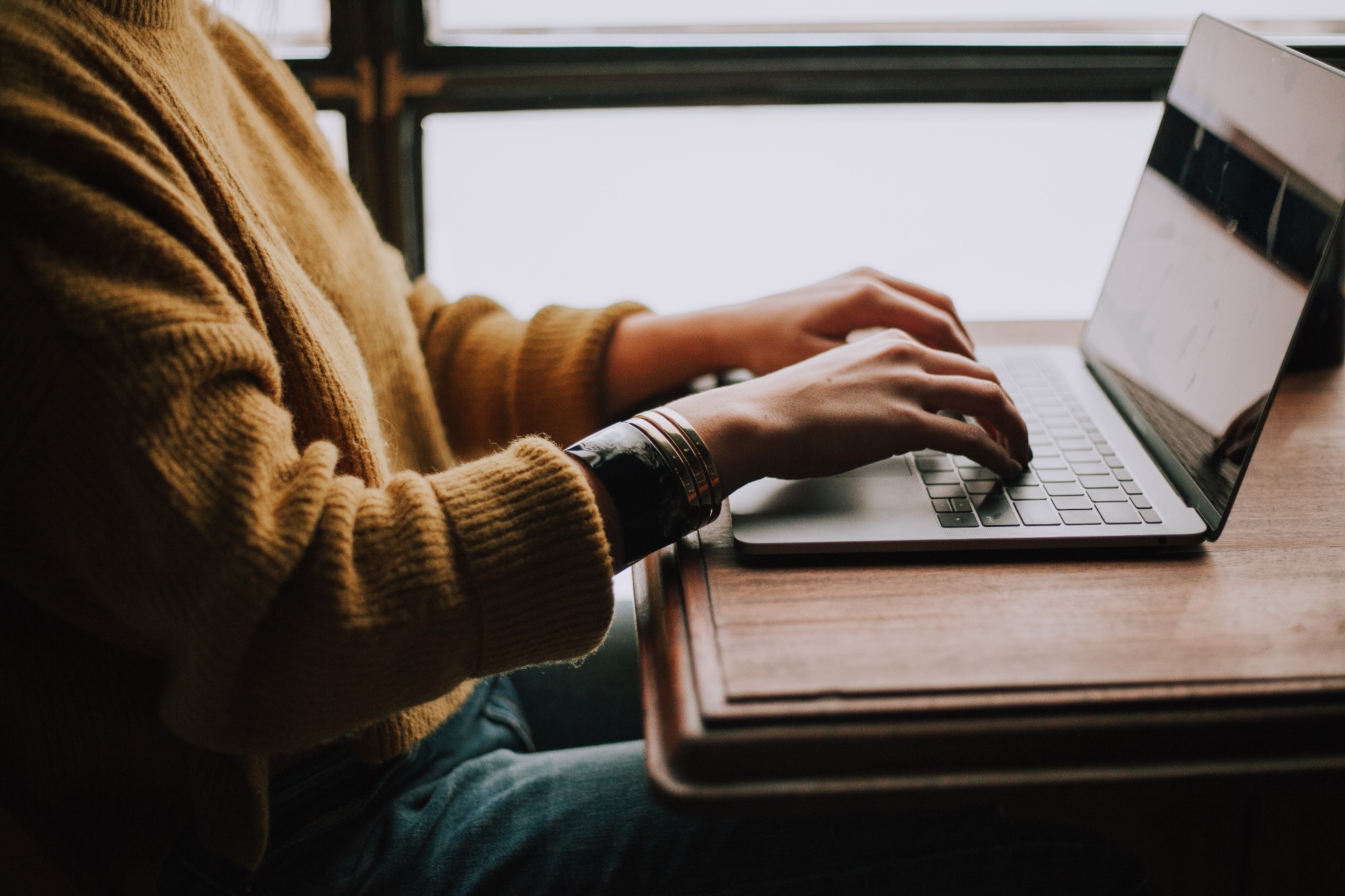 A person in a yellow sweater types on a laptop.