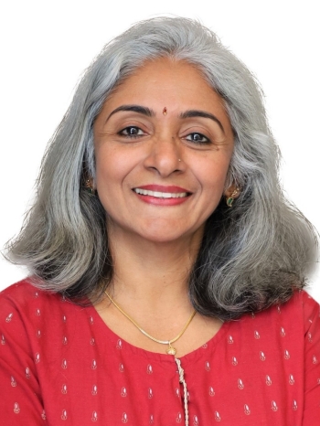 Sobhana is a South Asian woman who has gray hair and dark brown eyes. She is wearing a red shirt and is smiling at the camera.