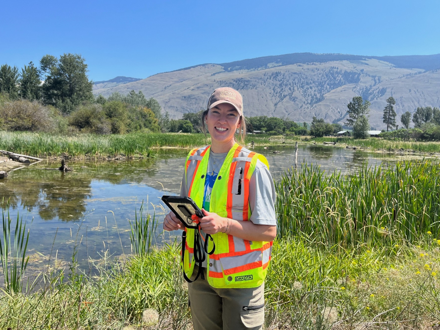 Emma standing in a wetland, smiling at the camera in a high vis vest 