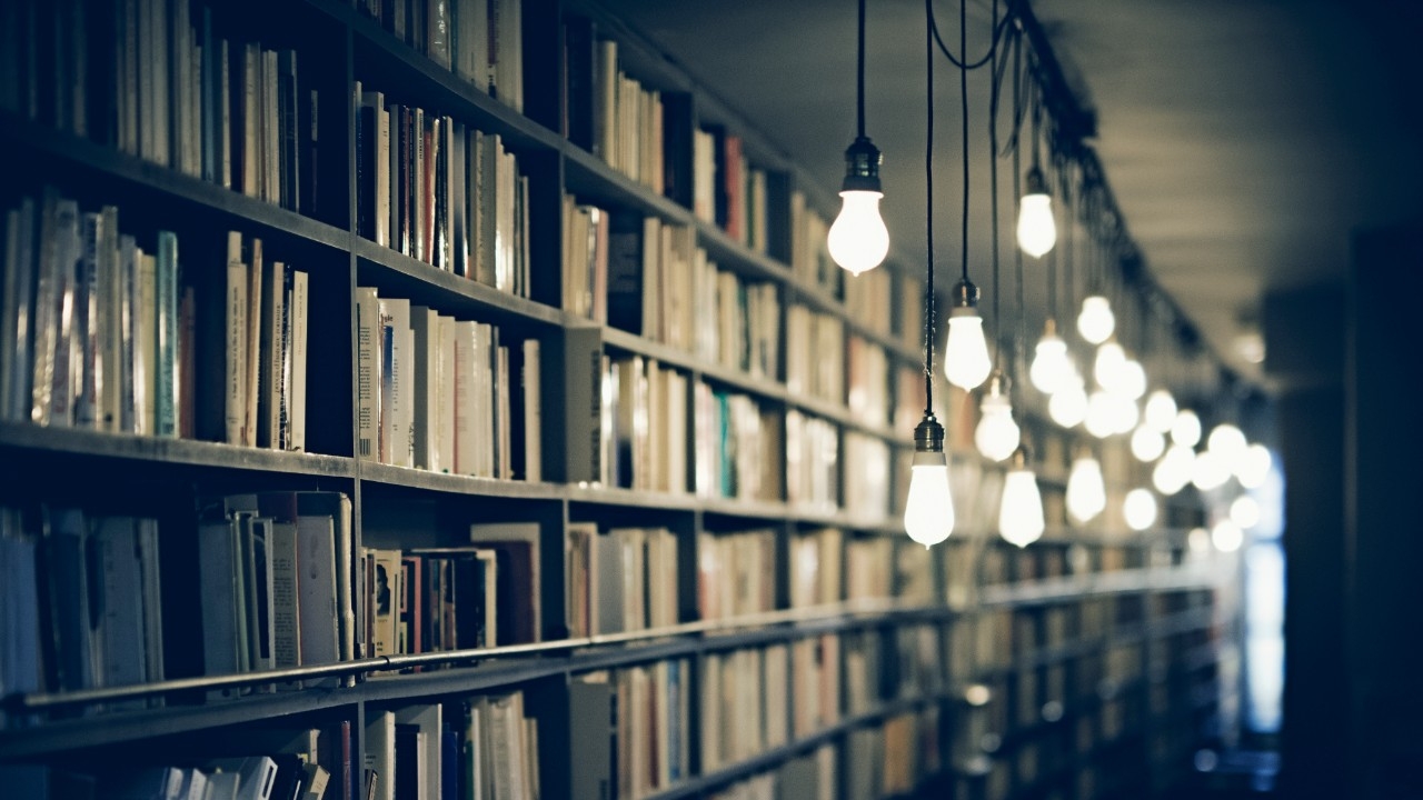 A library with filled bookshelves and blurred light bulbs hanging from the ceiling. Original public domain image from Wikimedia Commons