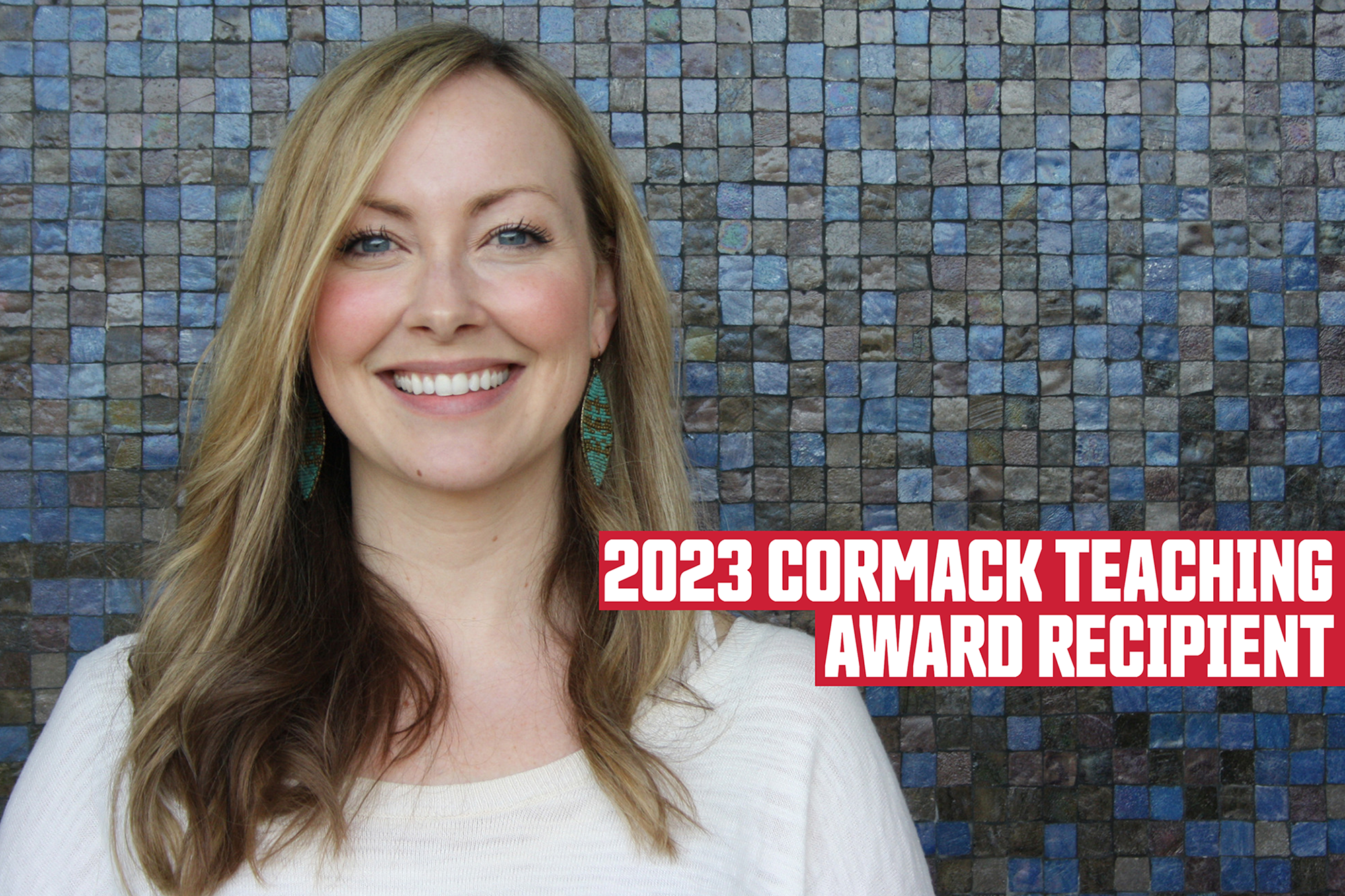 2023 Cormack Teaching Award Recipient; Photo: Coleman Nye, a smiling woman with blonde hair, standing in front of a tiled wall