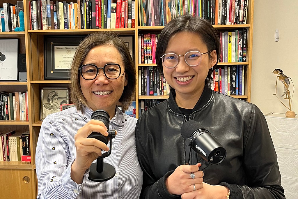GSWS faculty members Helen Leung and Carman Fung, standing together smiling and holding microphones