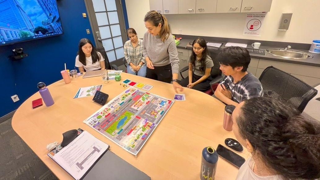 View of conference room with a draft print of game placed on the table, and six researh assistants having a discussion about it.