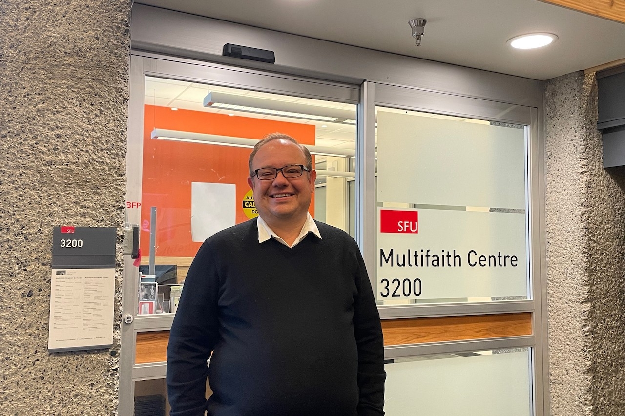 Seth Greenham smiles in front of the Multifaith Centre entrance.