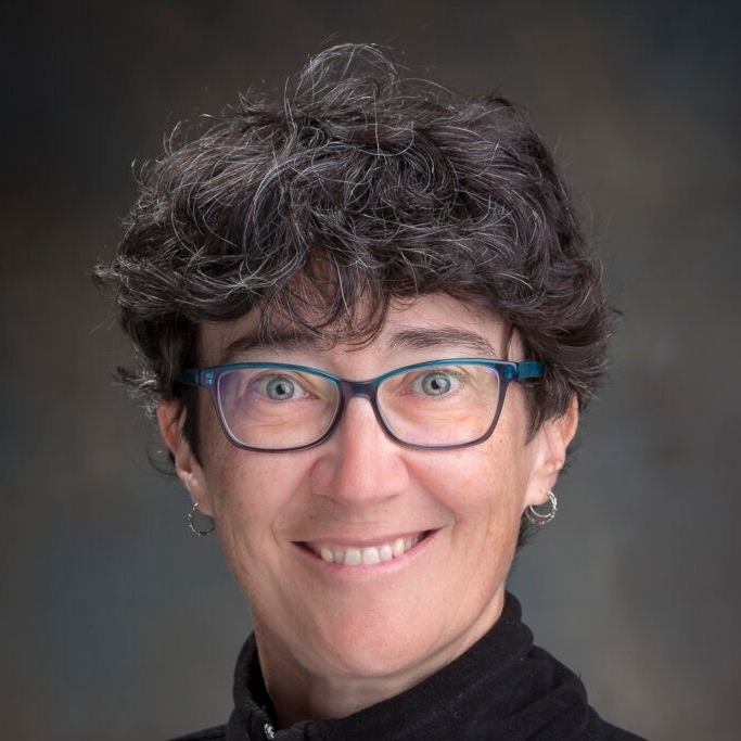 Petra Menz smiling in front of a gray background.