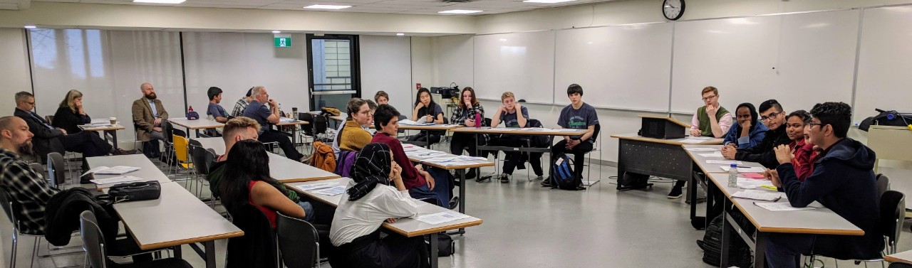 two teams seated at tables in front of an audience in an Ethics Bowl competition