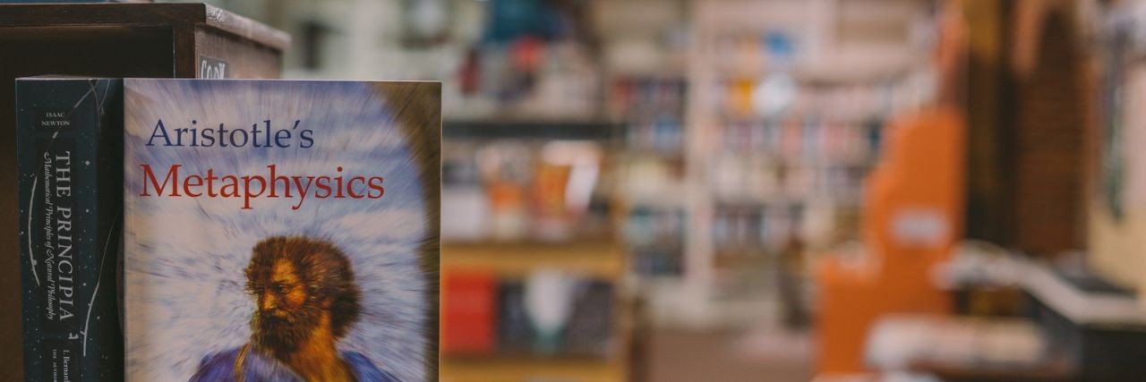 Books on a shelf in a library, with a focus on a copy of Aristotle’s Metaphysics
