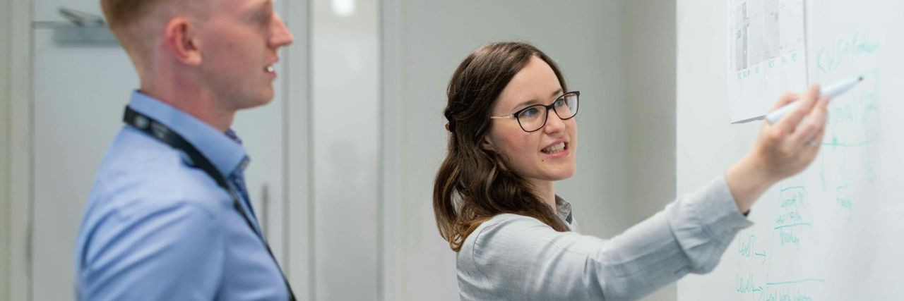 Two people standing at a whiteboard during a discussion in a professional setting
