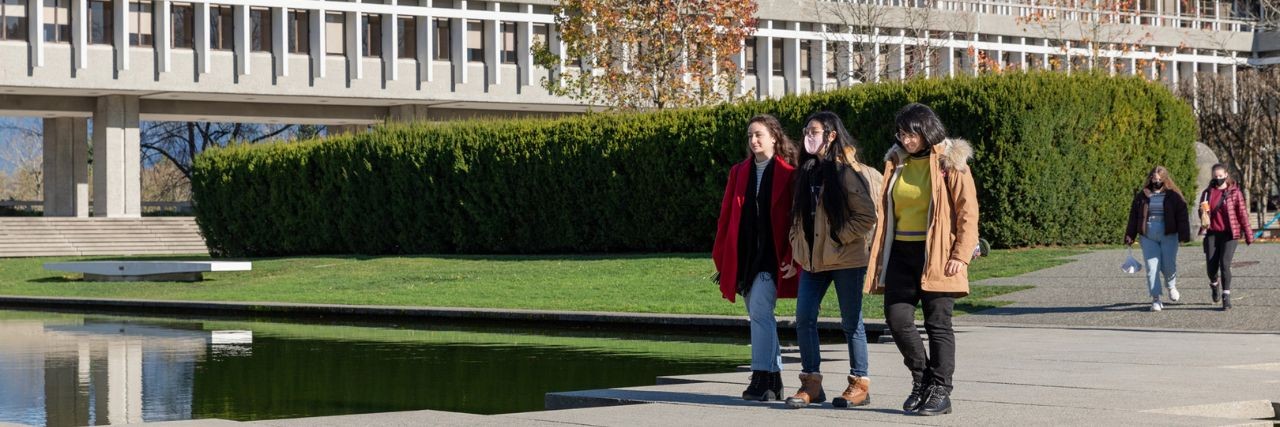 Three students walk by the reflecting pool at Simon Fraser University.