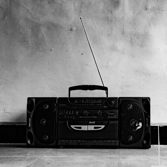 An older radio is shown on the ground, pressed against the wall, with an antenna up to receive a signal. 