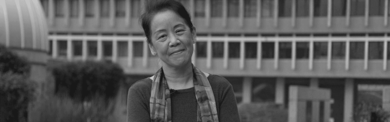 Black and white banner photo of Kelley Lee with SFU Burnaby Campus behind her. The top left reads, "President's Faculty Lecture" and the top right features the SFU Public Square logo