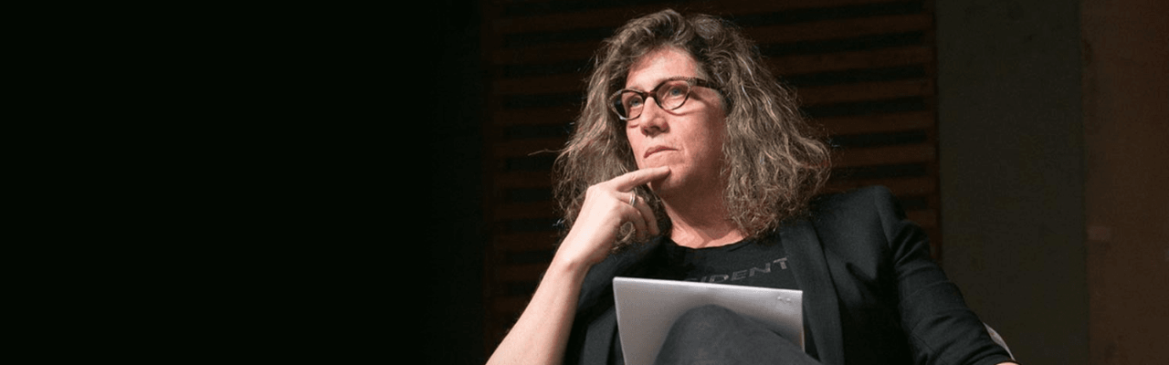 Dr. Susan Stryker sits on a stage with hand to chin