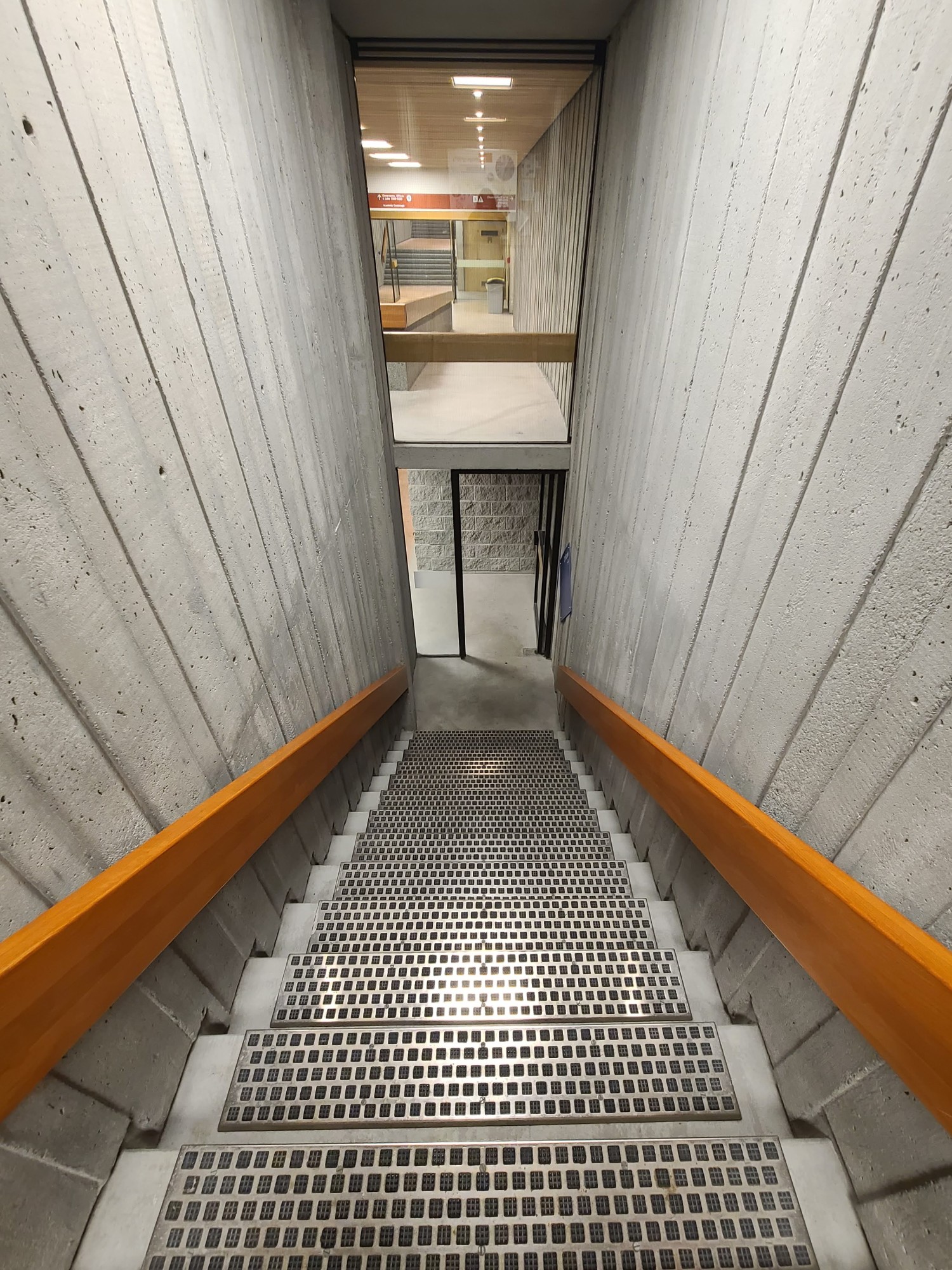 A grey metal staircase leading downward, surrounded by walls of concrete.