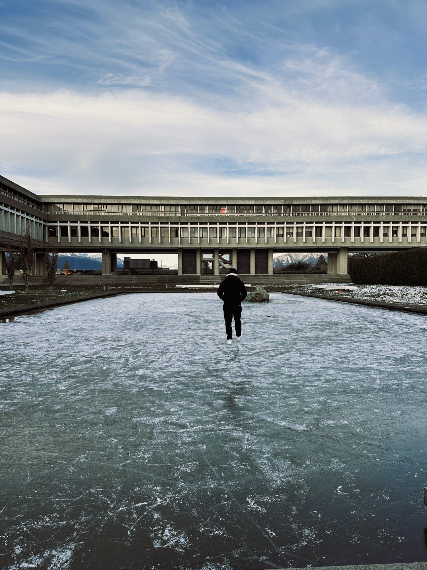 The pond of SFU Burnaby frozen in the winter and above the ice walks a student.