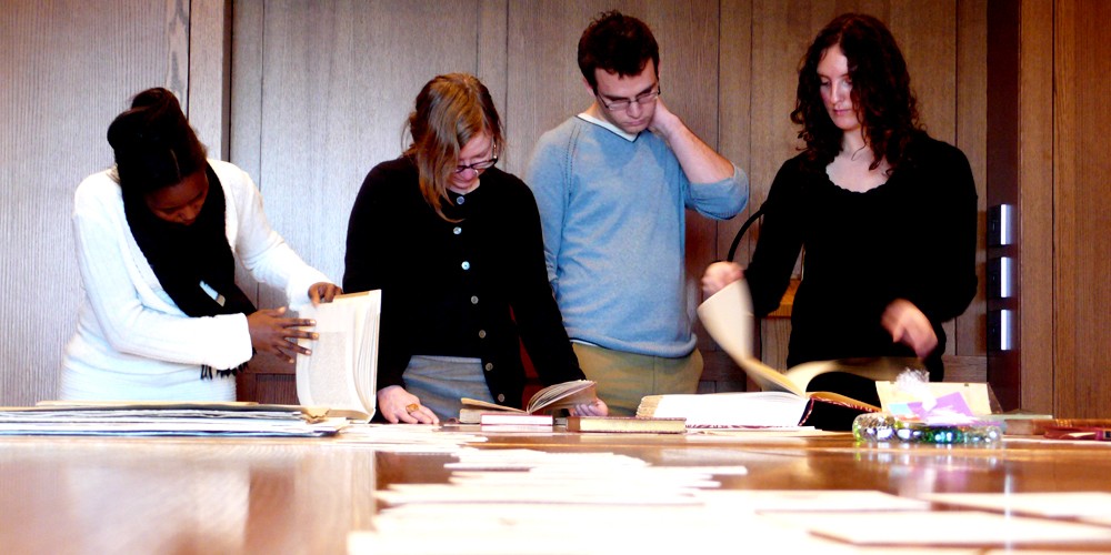 Four people looking through books and piles of papers