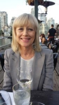 A smiling woman with blonde hair, wearing a suit, sitting outdoors at a restaurant