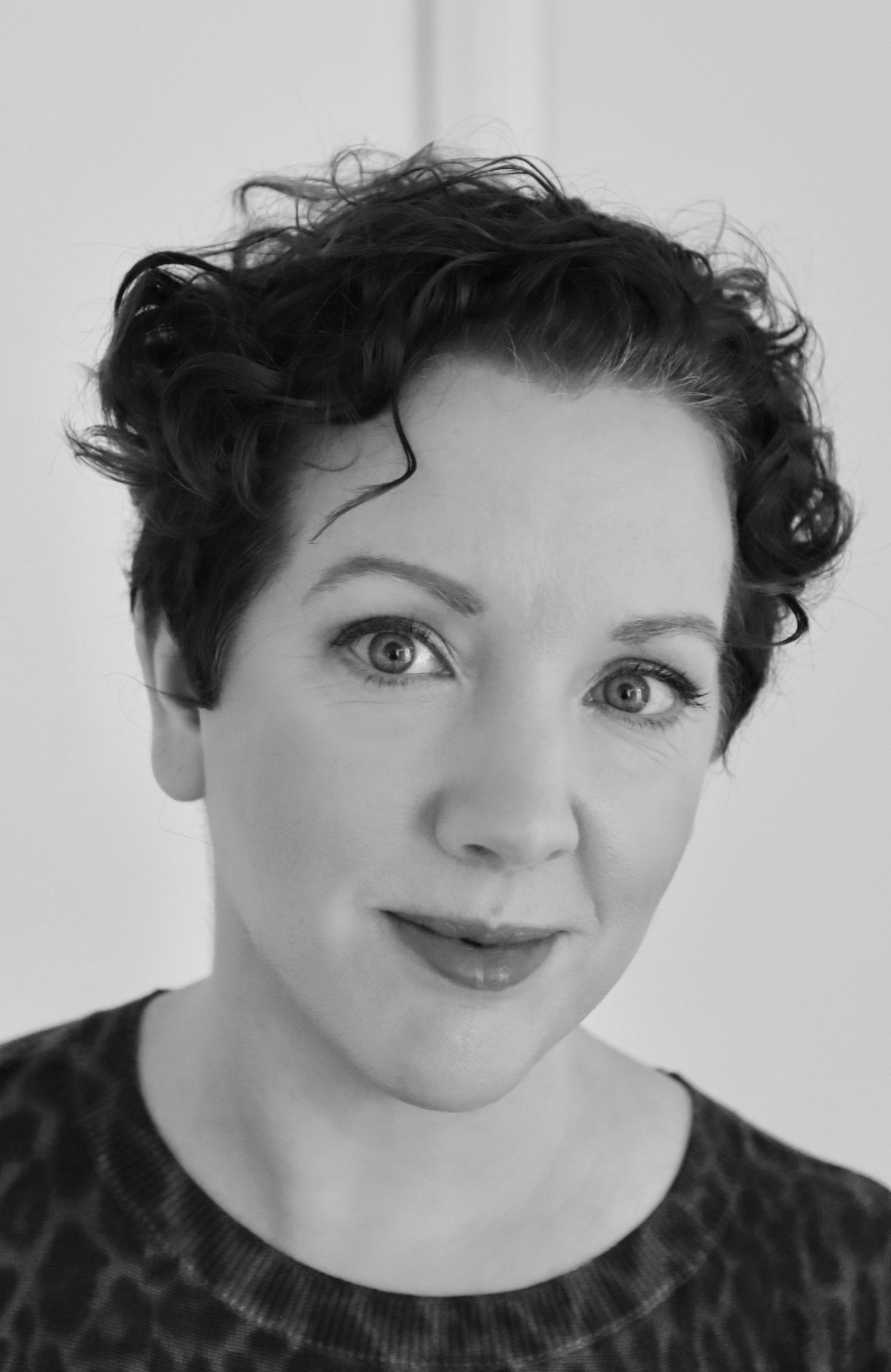 A striking black and white headshot of Master of Publishing (MPub) alumna Claire Cavanagh. Claire has wavy dark pixie-cut hair and is gently smiling towards the camera. 