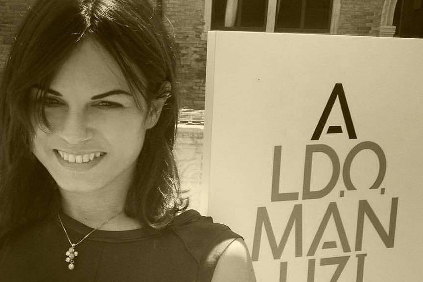 Alessandra smiles as she poses in front of an exhibition (“Aldo Manuzio. Il rinascimento di Venezia”) poster in Venice.