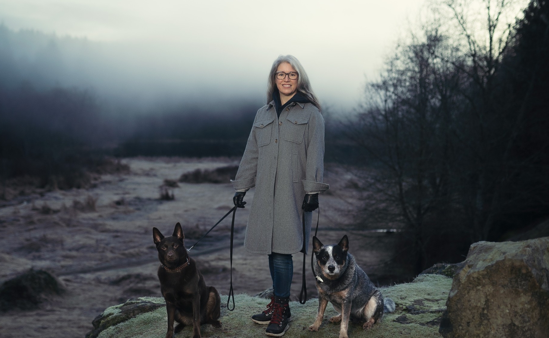 MPub alumna and author Susan Juby's pictured with her two dogs on a small barren hill.