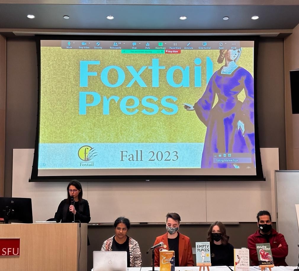 Five SFU Master of Publishing (MPub) students presenting (behind them) the cover of their group’s press catalogue: A yellow graphic that reads Foxtail Press in white and beside it is a full lengthy display of one of their title characters; Emilia. Underneath the bold text is the Press’s logo which is a partial yellow circle encompassing the letter f in black. It is grounded in what appears to be black grass vector art. A black line separates the logo from the text Foxtail.