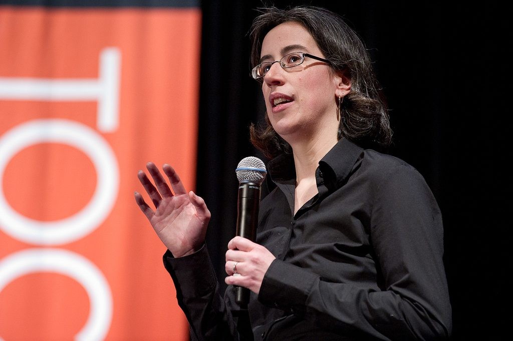 A woman with short dark hair and glasses speaking on a stage