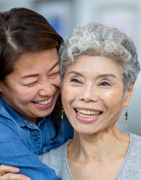 an older adult asian woman being hugged by her daughter