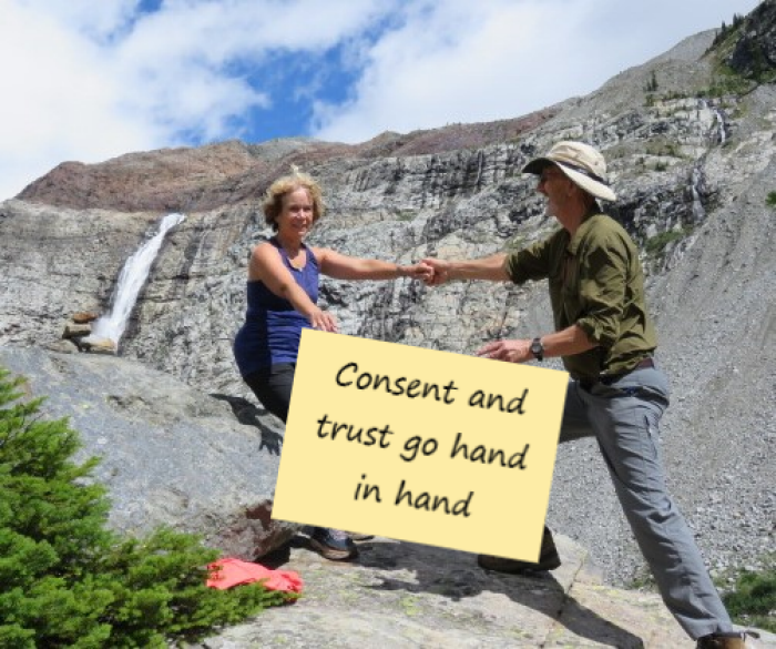 Two people holding hands on a cliffside, and a sign together that reads: "Consent and trust go hand in hand."