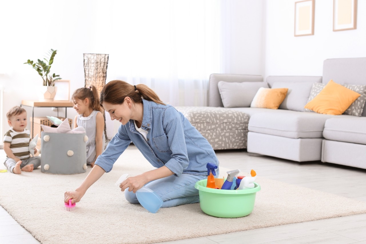 Housewife cleaning carpet while her children playing in room