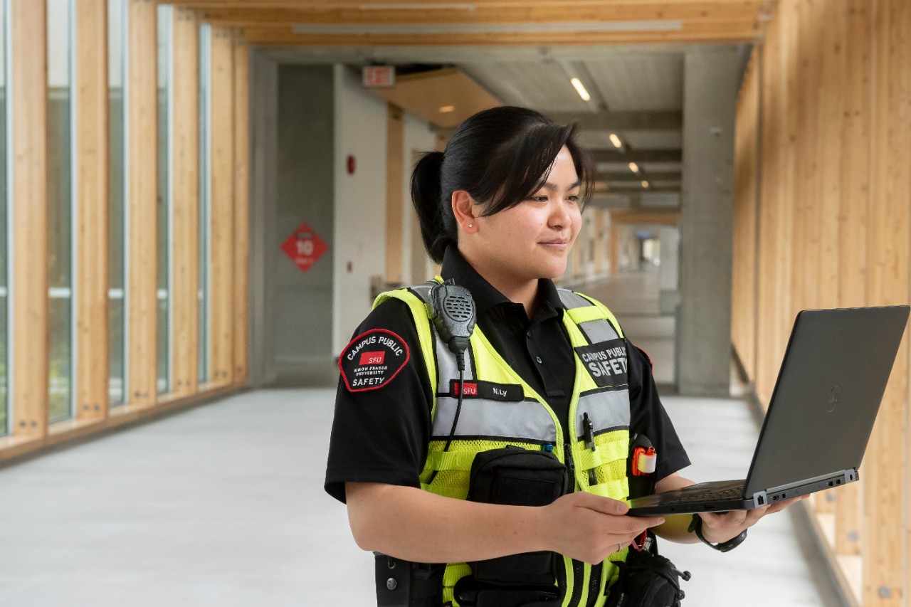 Nicole Ly, security supervisor and residence liaison with Campus Public Safety, poses in her uniform with a laptop.