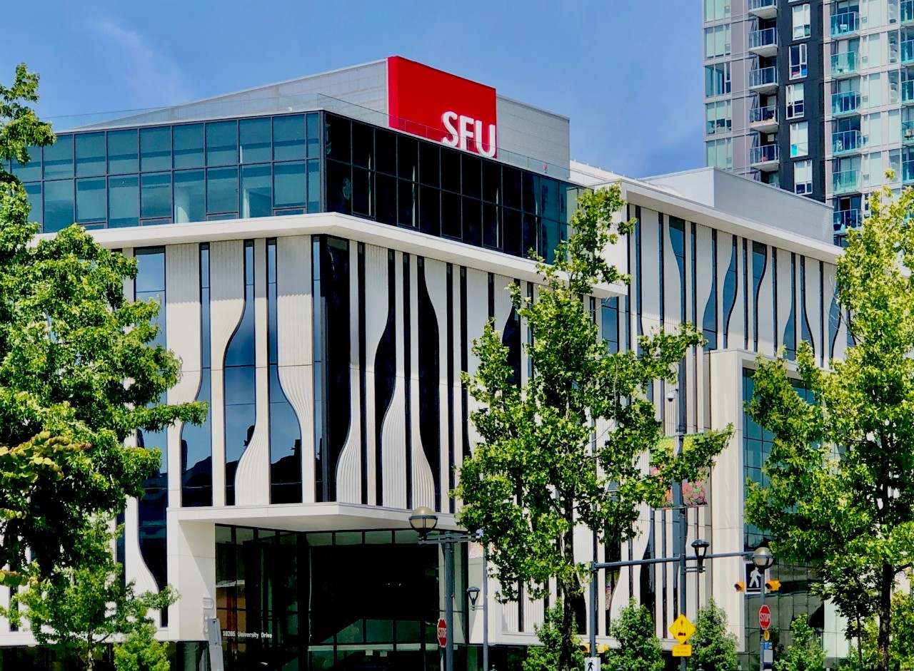 A white and blue building on a sunny day. The building has a red SFU sign on top of it.