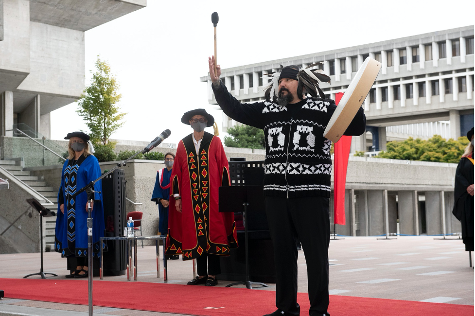 Gabriel George, director of treaty, lands and resources for the Tsleil-Waututh Nation, opened the Fall 2020 Installation Ceremony with traditional drumming and singing. SFU Chancellor Tamara Vrooman and President Joy Johnson stand behind, wearing their redesigned regalia.