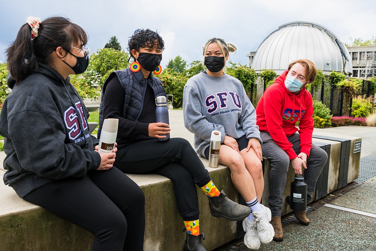 Four SFU students wearing masks and smiling as they hold on their reusable bottles