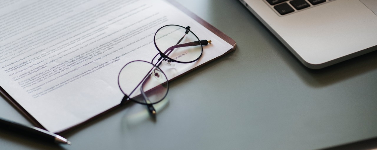 photo of a desk with a laptop, reading glasses and a contract