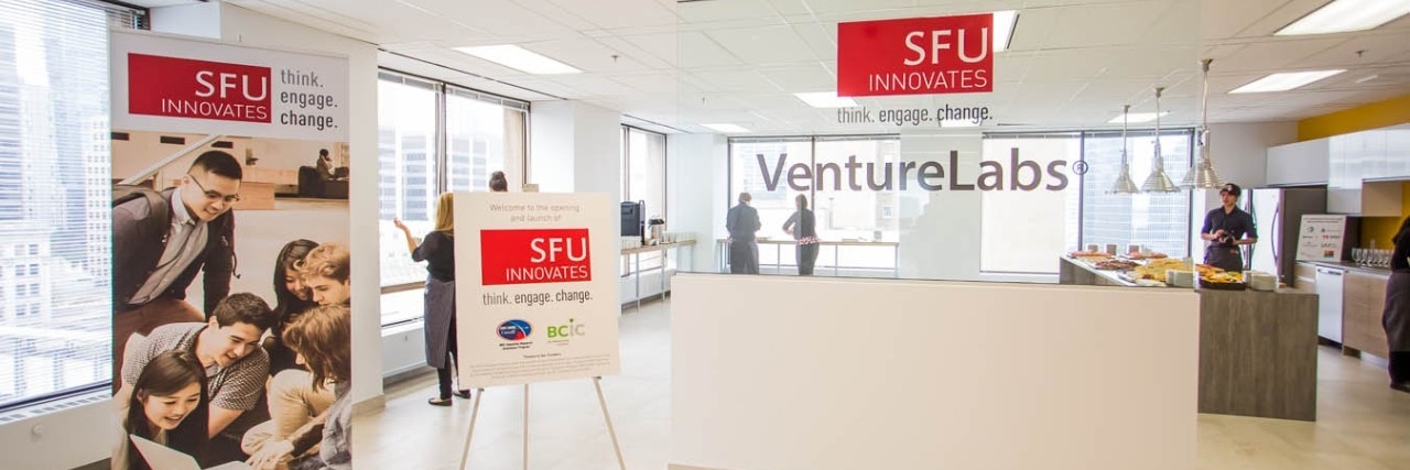 Front entrance to VentureLabs® office space with people standing in one the office's common areas and kitchen