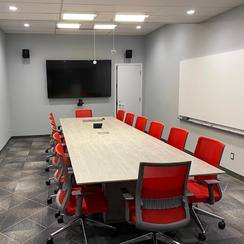 Small, enclosed meeting space with table, chairs, whiteboard, and monitor