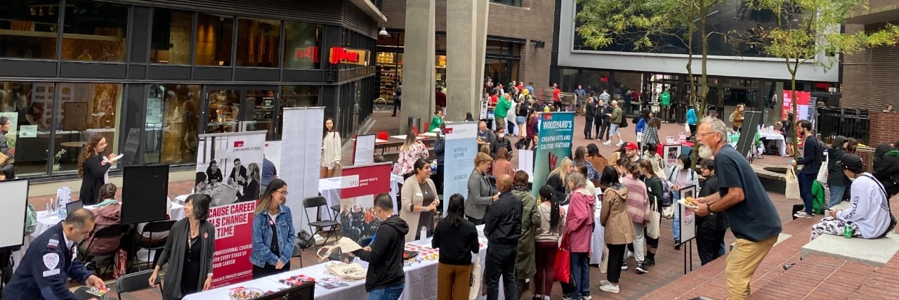 Vendors set up outdoors with multiple people visiting the various vendors' tables at a Welcome Back Community BBQ