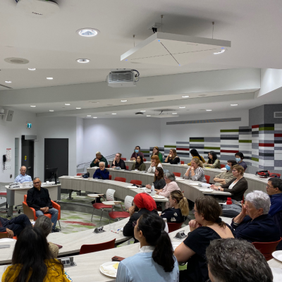 Multiple people sitting in a room with rows of tiered seating set in a semi circle listening to the speakers at an SFU Vancouver Lunch 'n' Learn event 
