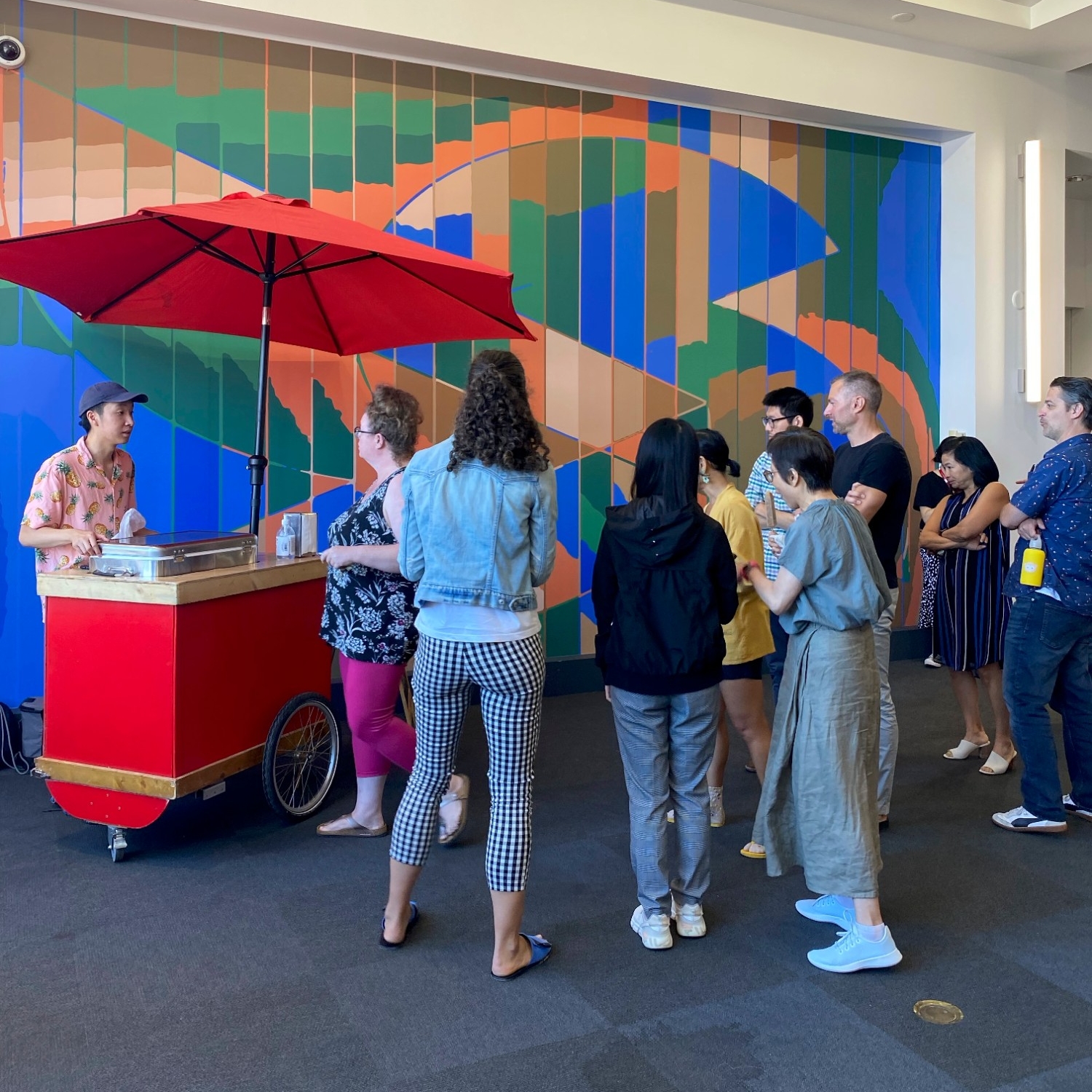 Multiple people lined up for popsicles against a wall with a colourful mural at the 2023 Summer Social
