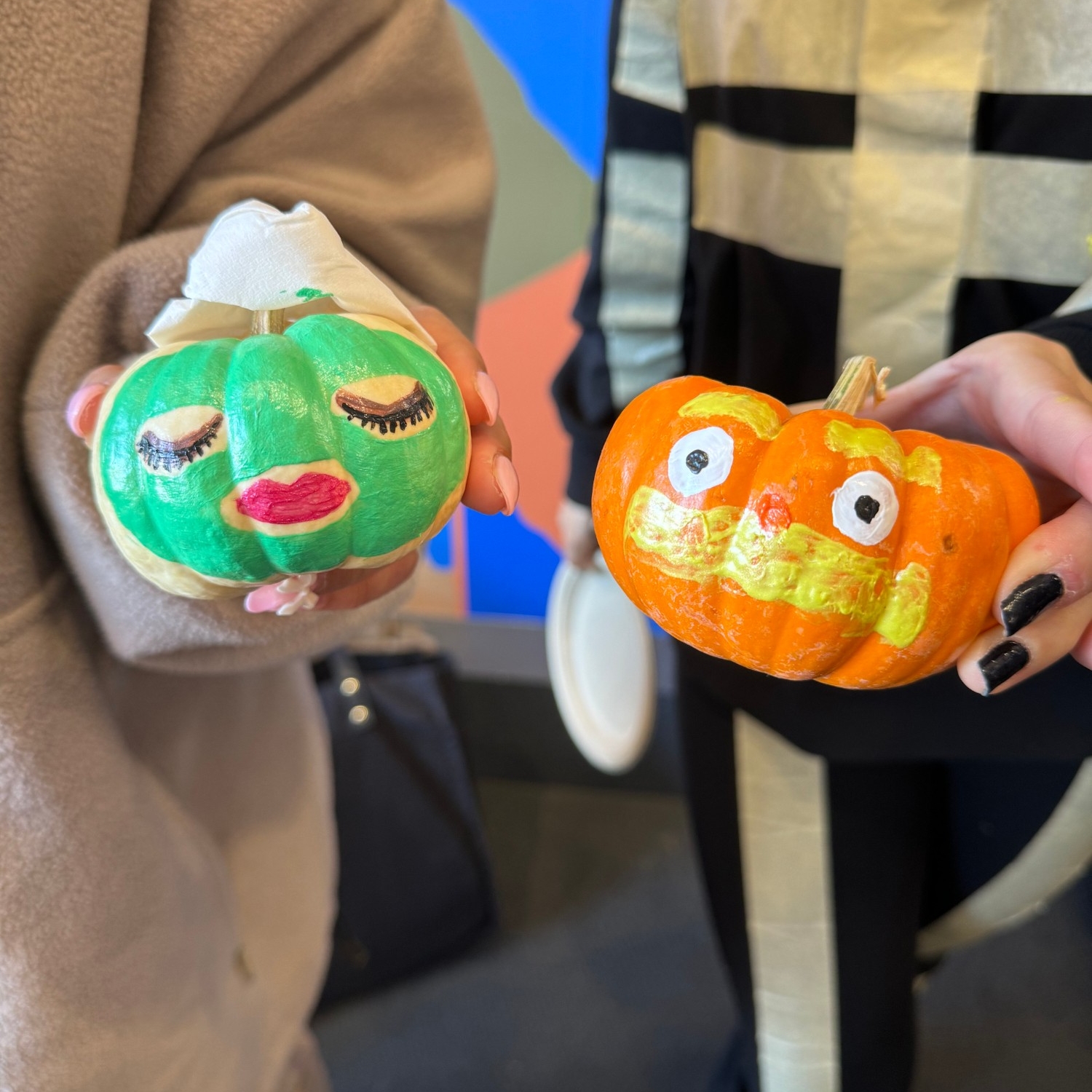 Two hands holding the mini pumpkins they painted at 2023 Halloween Social