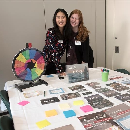 Two people hosting a table at an event, with health resources and trivia wheel on the table