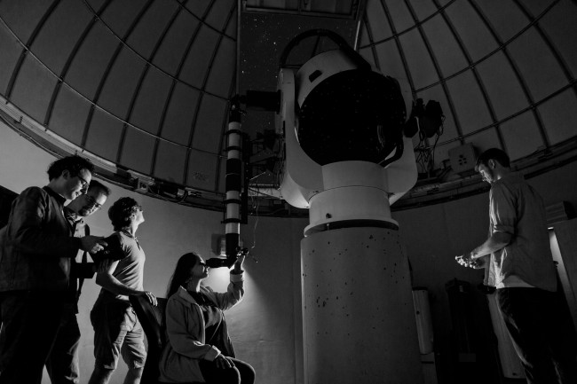 Black and white photo of 5 researchers gathered around a telescope. 