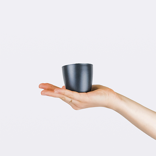A hand holding a small black plant pot. This image links to Daen (Small)'s product details page.