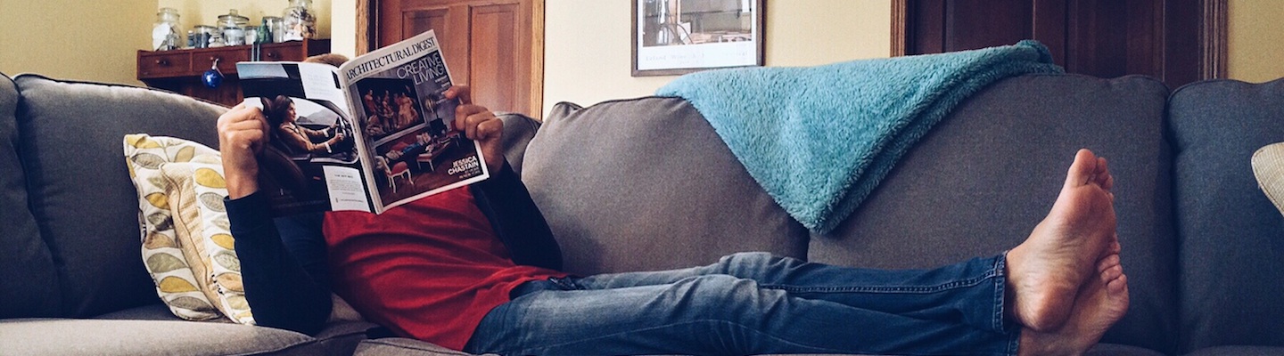 Banner image of a man lying down on a couch and reading a newspaper